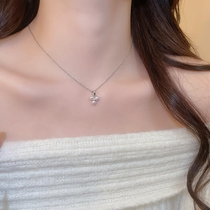 Close-up of a delicate silver pearl clover pendant necklace on a model's neck