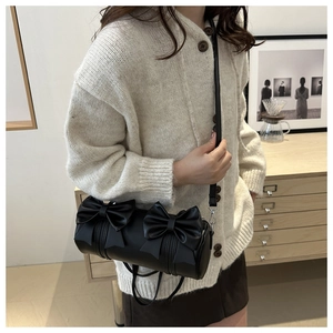 Detail of black cylindrical shoulder bag featuring PU leather and double bow accents