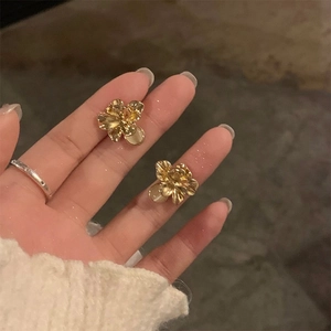 Elegant gold flower stud earrings with pearl centers held between fingers