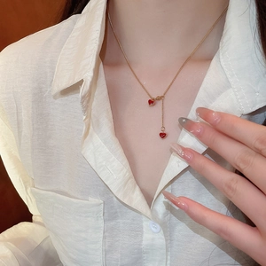 Close-up of a gold Y-shaped necklace with red heart pendants worn on a white shirt