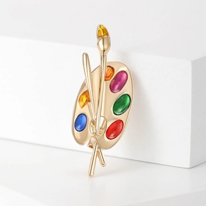 Artistic palette brooch pin in gold metal with colorful stones on white background