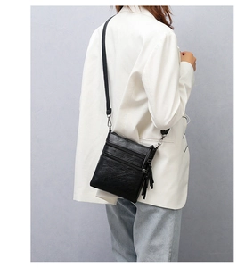 Close-up of black leather crossbody phone bag with three zippers and stylish long tassel
