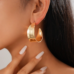 Close-up of a model wearing chunky gold geometric C-shaped hoop earrings with mirror finish