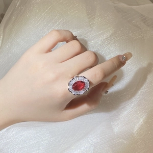 Detail view of a luxury red oval gemstone ring with sparkling zircon halo on finger