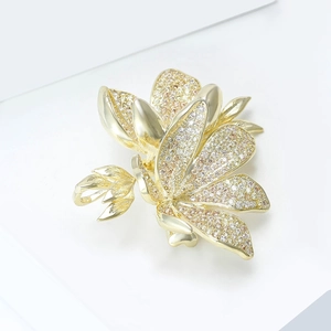 Macro detail of golden flower brooch with micro-paved white and champagne zircons