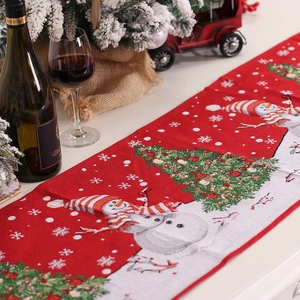 Christmas table runner with red embroidery featuring snowmen and festive trees on white table