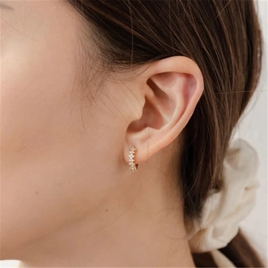 Close-up of a model wearing sparkling gold hoop earrings with row-set white zircons