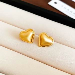 Macro shot of gold-plated heart earrings with brushed metal texture and polished edges