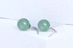 Macro detail of natural green aventurine ball earrings on a minimalist white stone base