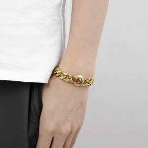 Golden Cuban link bracelet with a faceted red gemstone worn on a male model wrist