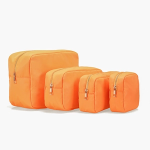 Detailed set of four orange nylon cosmetic bags in various sizes with gold zippers