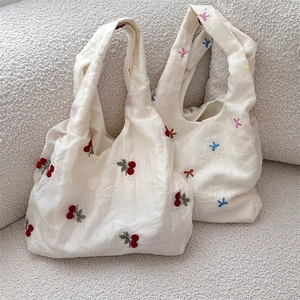 Detail of white embroidered tote bags with cherry and bow patterns on textured fabric