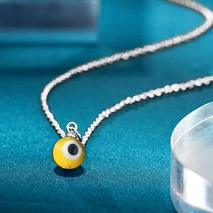 Macro shot of a yellow evil eye pendant with blue details on a silver twist chain