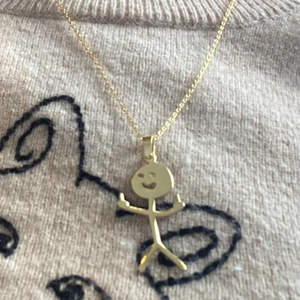 Detail shot of a golden funny doodle stickman necklace resting on a beige knit sweater