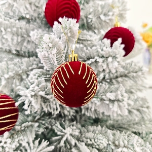 Boule de Noël en velours rouge avec motifs dorés sur un sapin de Noël floqué blanc
