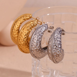 Hammered gold and silver J-shaped peanut shell earrings on a glass edge