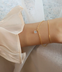 Close-up of double-layer gold chain bracelet with a single round cubic zirconia pendant