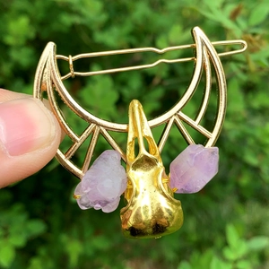 Golden hollow moon hair clip featuring a crow skull and purple crystals on a hand