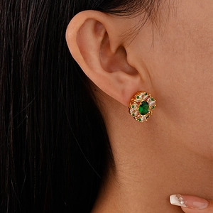 Close-up of vintage gold stud earrings with emerald green zircon and crystal floral details