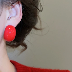 Close-up of bright red drop earrings with glossy finish on a model wearing a red sweater