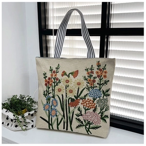 Detail of floral embroidery and striped handles on a cream canvas tote bag