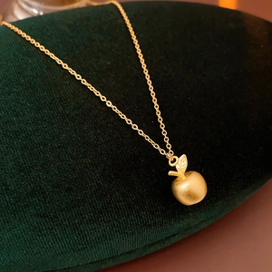 Close-up of matte 18k gold apple pendant necklace on a dark green velvet display