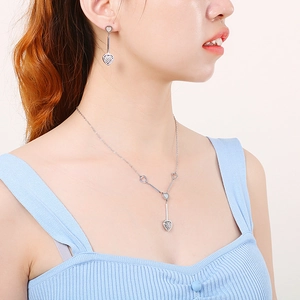 Elegant silver heart necklace and drop earrings set worn by a model in blue dress