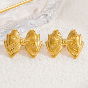Detail of 18k gold plated stainless steel bow earrings on textured white fabric