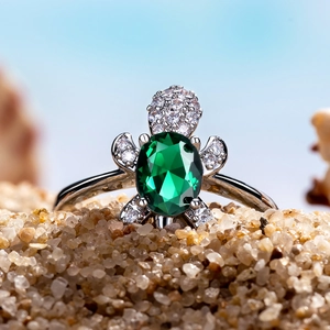 Macro shot of silver turtle ring with green oval gemstone nestled in beach sand