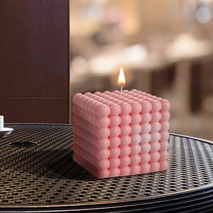 Candela a cubo rosa con stoppino acceso su un elegante tavolo in metallo nero