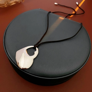 Detailed top view of a gold hollow double heart pendant on a black woven cord over a jewelry box