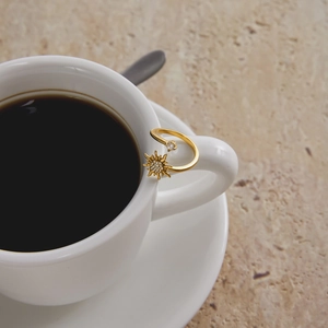 Close-up of a gold sun-shaped zircon ring elegantly placed on a white coffee cup handle
