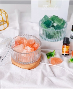 Pink crystal salt lamp with wooden base, glass bowl, and lemon essential oil bottles