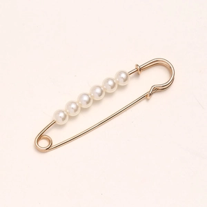 Golden waist pin with white pearls for clothing adjustment on a beige background