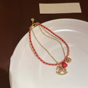 Detail of double-layer horse bracelet with red beads and golden rocking horse charm