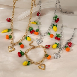 Golden and silver jewelry set featuring colorful fruit pendants on silk background