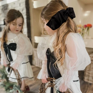 Detail of a large black satin bow headband worn by a child in a home setting