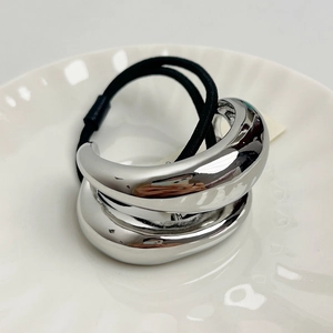 Polished silver crescent metal hair tie on a white ceramic dish with elastic band detail