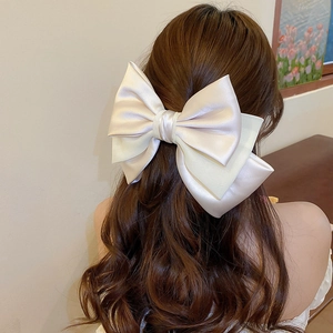 Detail of oversized cream satin bow hair clip styled on long wavy hair from behind