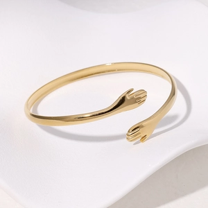 Detailaufnahme des goldenen Edelstahl-Armreifs mit Hände-Umarmung-Design in Gold
