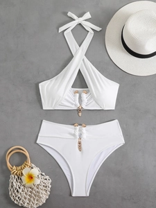 Close-up of white bikini with gold lion charms and high-waisted bottoms on grey background