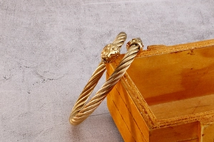 Détail macro du bracelet tressé à tête de loup doré sur un présentoir en bois
