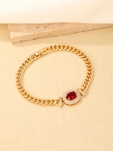 Macro shot of gold curb link bracelet with red oval gemstone and zircon pavé detail