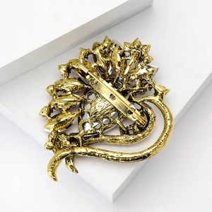 Elegant gold crystal heart brooch with leaf motifs on a modern minimalist pedestal