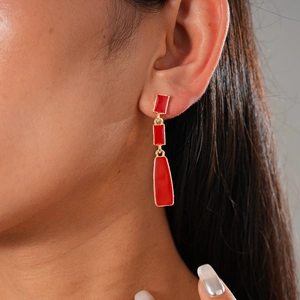 Close-up of triple geometric red resin earrings with gold trim worn by a model