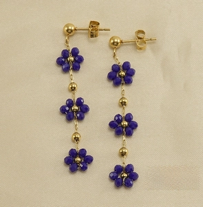 Detail of long gold earrings featuring three layered purple crystal flowers with gold beads