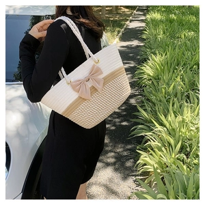 Outdoor model holding woven tote bag in cream white with large bow and rope handle