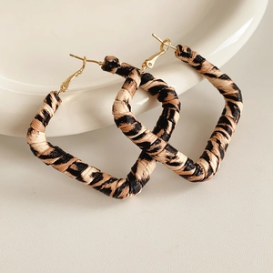 Detailed view of square leopard print fabric earrings with gold hooks on a white ceramic plate