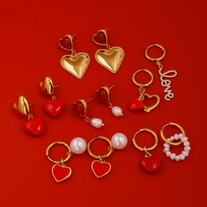 Detailed arrangement of gold heart earrings with red enamel and pearls on red background