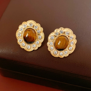 Dettaglio di orecchini a fiore dorati con pietra occhio di tigre e cristalli brillanti